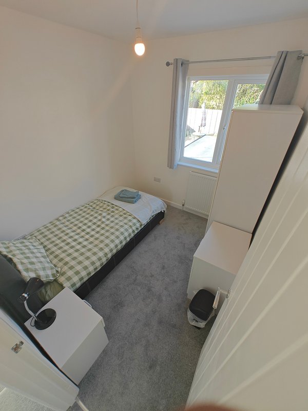 Small bedroom with single bed, pendant light, window, and white furniture storage