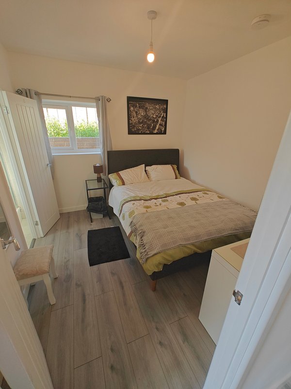 Compact bedroom with double bed, wooden flooring, window with curtains and pendant light
