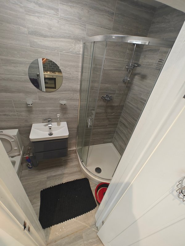 Modern bathroom with grey tile walls, shower enclosure, white sink, round mirror and black mat