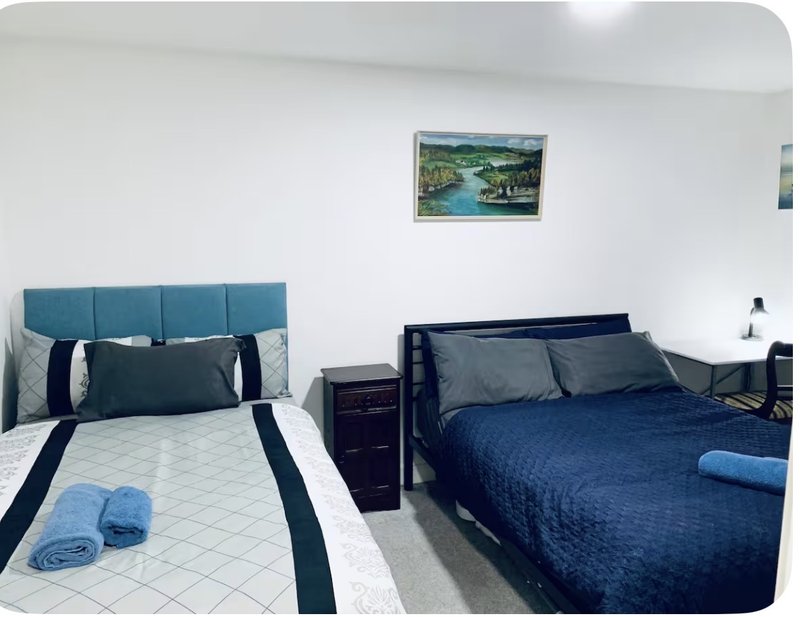 Bright bedroom with two single beds, blue headboards, white bedding and dark blue quilts