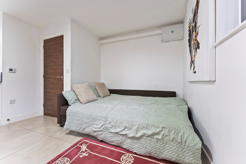 Bright bedroom with double bed, green bedding, red rug, wooden door and tiled floor