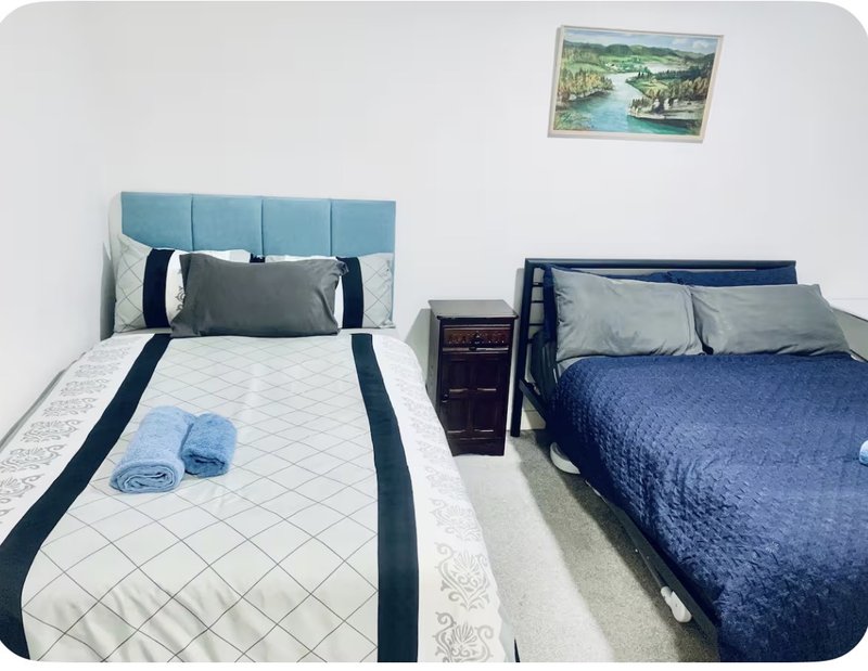 Twin bedroom with two beds, blue headboards, rolled towels, and framed landscape artwork on wall
