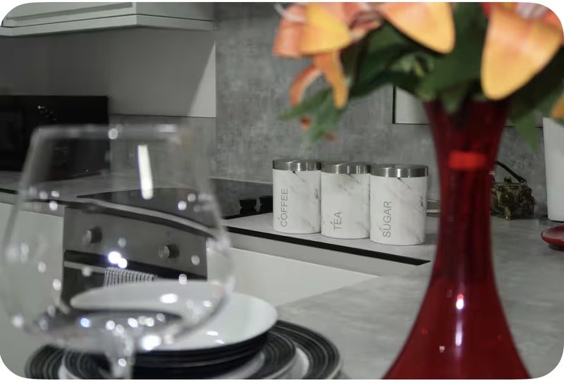 Modern kitchen counter with appliances, storage containers, and flowers in a red vase