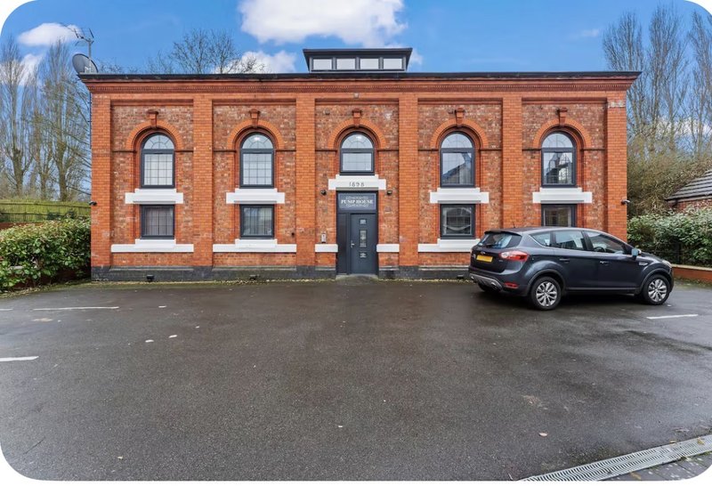 Red brick building exterior with parked car, driveway and bare trees
