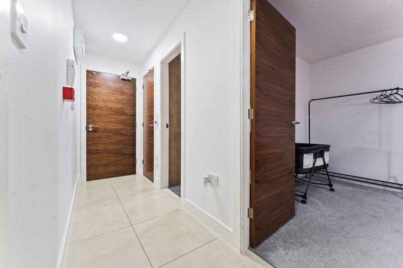 Bright hallway with cream tile flooring, white walls, wooden doors and open doorway to carpeted room