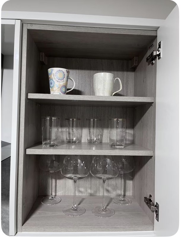 Open kitchen cabinet with mugs, glasses and stemware arranged on three shelves