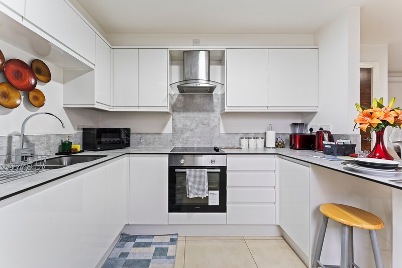 Modern white kitchen with black countertops, built-in oven, and decorative plates on wall