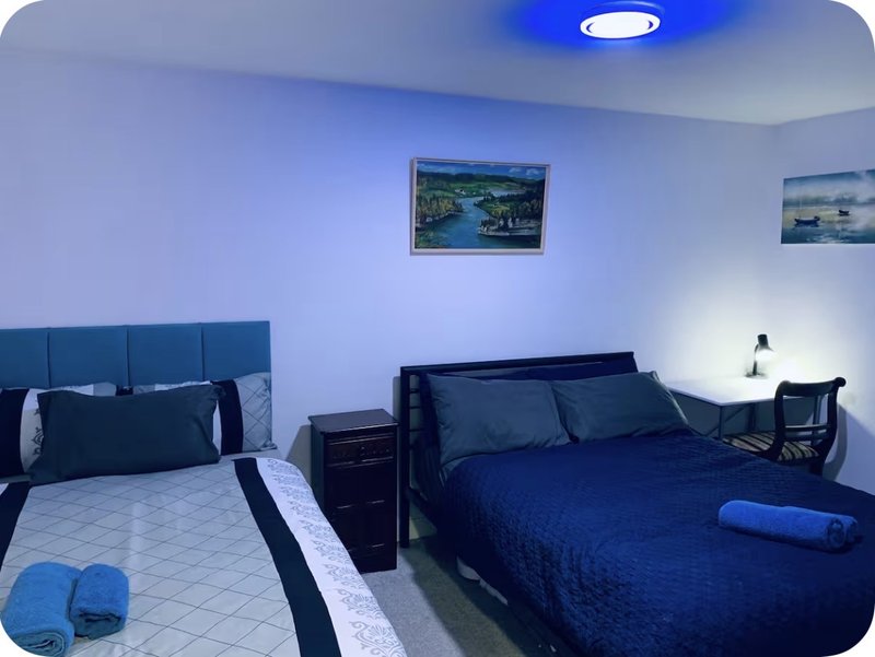 Bedroom with two beds, blue bedding, framed landscape prints, and modern lighting