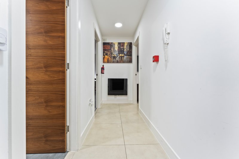 Bright hallway with wooden door, tiled floor, wall art and recessed lighting