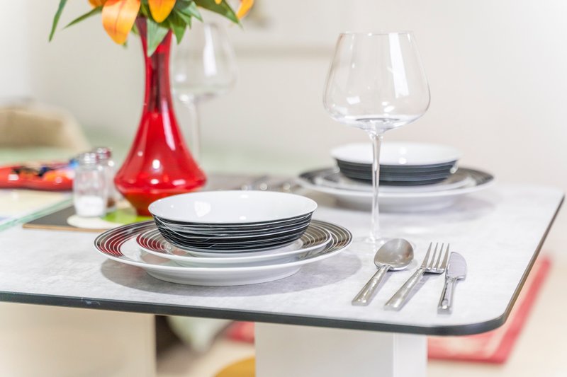 Formal dining table setting with stacked plates, glassware, cutlery and red vase of flowers