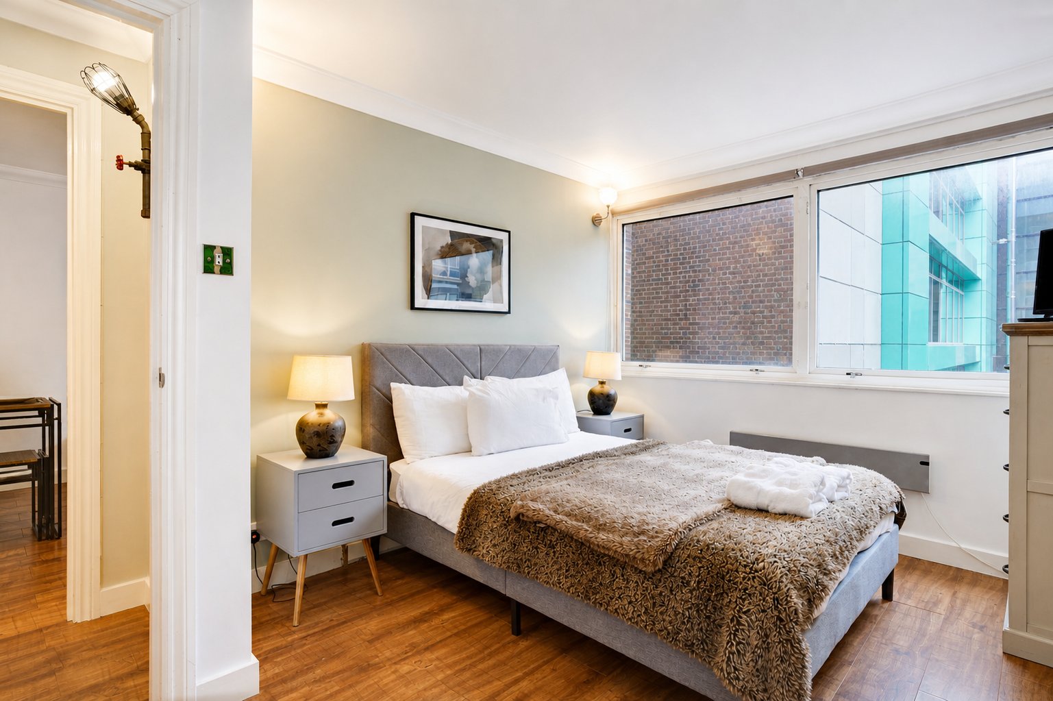Modern bedroom with double bed, grey headboard, bedside lamps, wooden flooring and large window