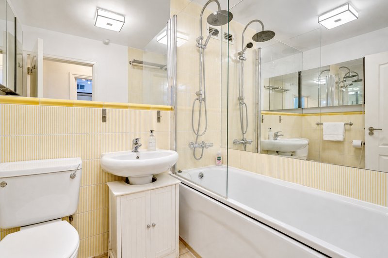 Bright bathroom with yellow tile walls, white vanity sink, toilet, bathtub and shower enclosure