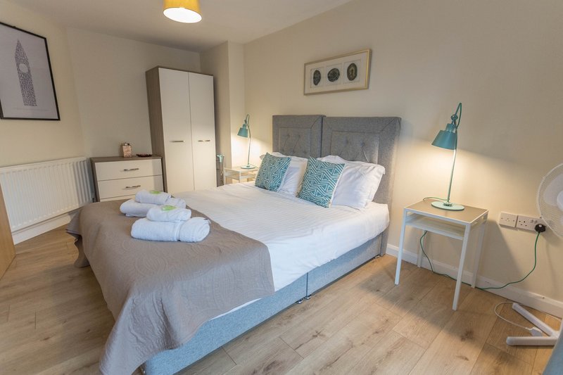 Bedroom with double bed, grey headboard, white wardrobe, wooden floor and bedside lamps