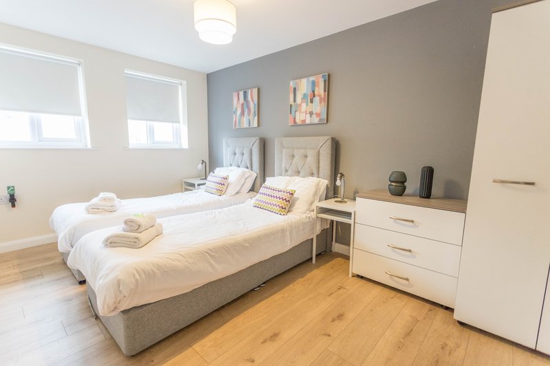 Modern bedroom with two single beds, white dresser, wooden floor and bright windows