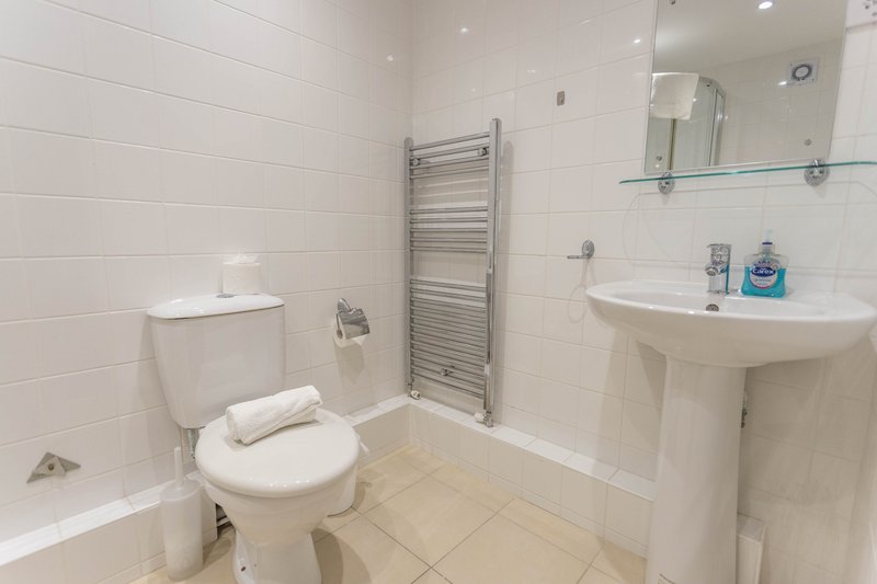 Modern bathroom with white tiles, toilet, pedestal sink, heated towel rail and mirror