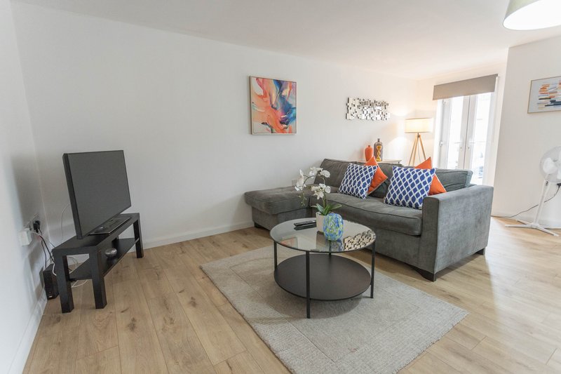 Bright living room with grey sofa, television, round coffee table and wooden flooring