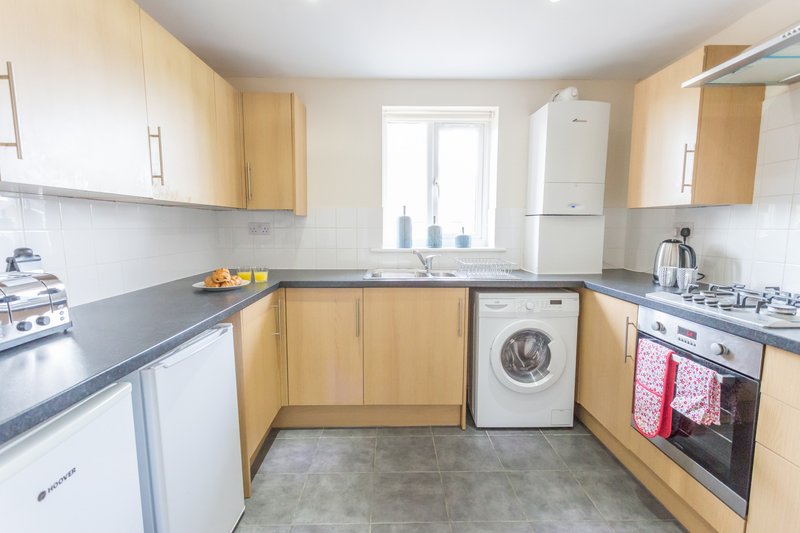 Modern kitchen with light wood cabinets, dark countertops, integrated appliances and washing machine
