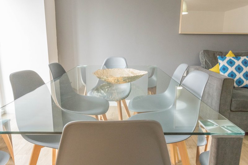 Modern dining area with glass table, grey chairs, wooden legs and decorative cushions