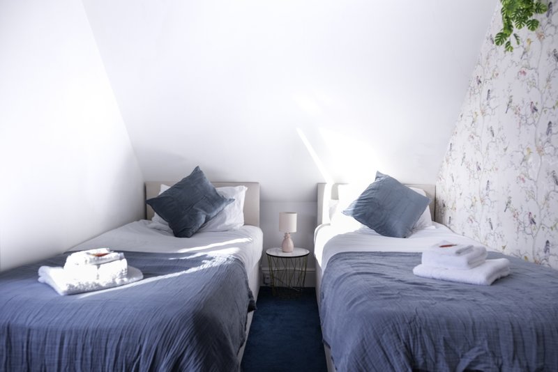 Twin bedroom with two single beds, dark blue bedding, dark cushions, and white towels