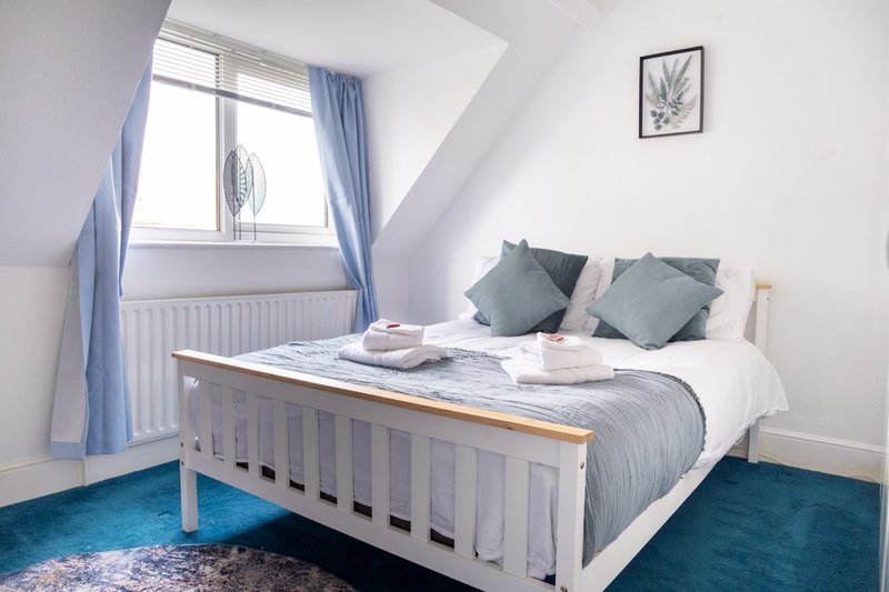 Bright attic bedroom with white wooden bed, blue cushions, teal carpet and sloped ceiling