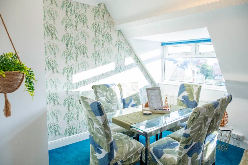 Bright attic dining nook with patterned wallpaper, table, chairs and hanging plant