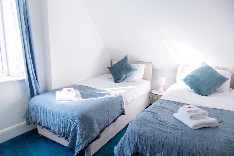 Twin bedroom with blue bedding, pillows, white walls, and bright window light