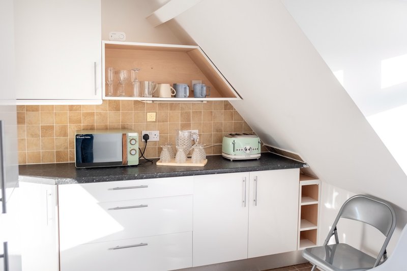Compact kitchenette with white cabinetry, black countertop, and beige tile backsplash under sloped ceiling