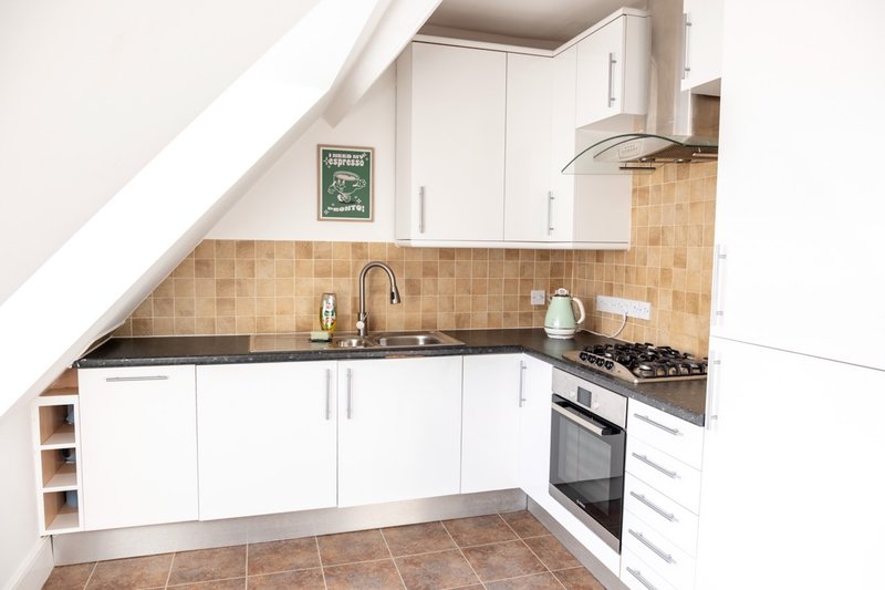Compact kitchen with white cabinetry, tile backsplash, gas stove, and sloped ceiling