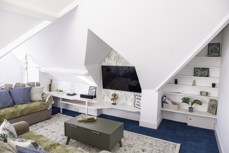 Attic bedroom with sloped ceilings, TV, shelving, seating area and natural light