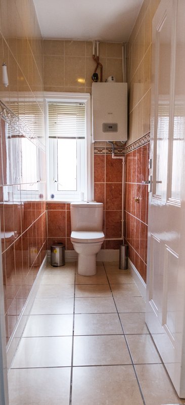 Small bathroom with toilet, sink, red tile walls, window, and boiler