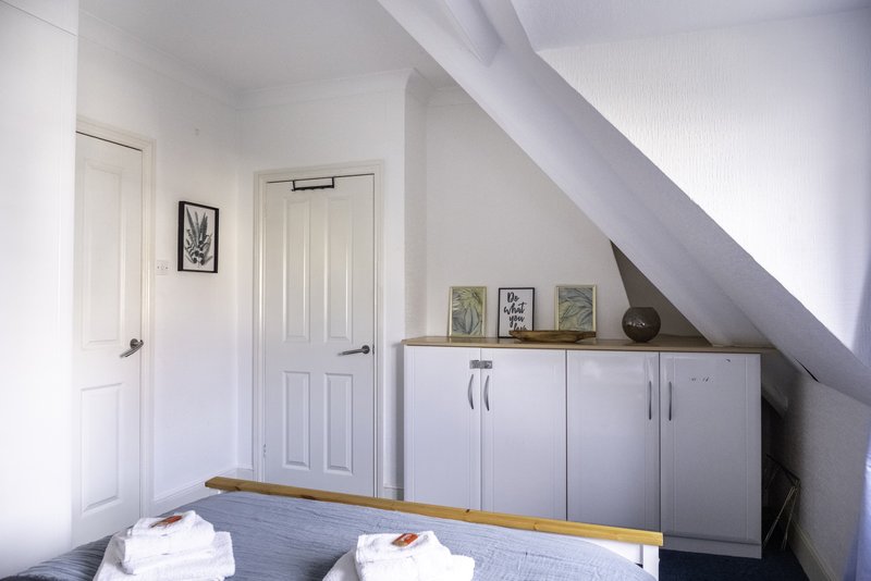 Bright attic bedroom with sloped ceiling, white doors, storage cabinet and framed wall art