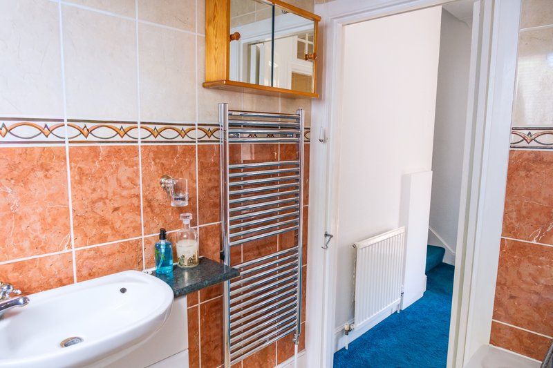 Bathroom with orange tile walls, white sink, mirror, heated towel rack and wooden cabinet