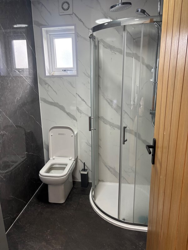Modern bathroom with toilet, curved glass shower enclosure, marble tiling and window