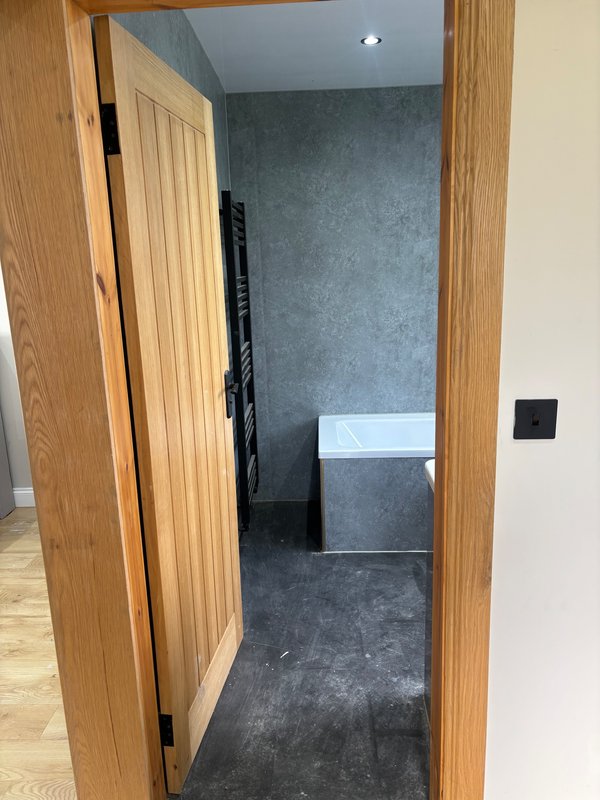 Modern bathroom with dark slate flooring, wooden door frame, white sink and fixtures