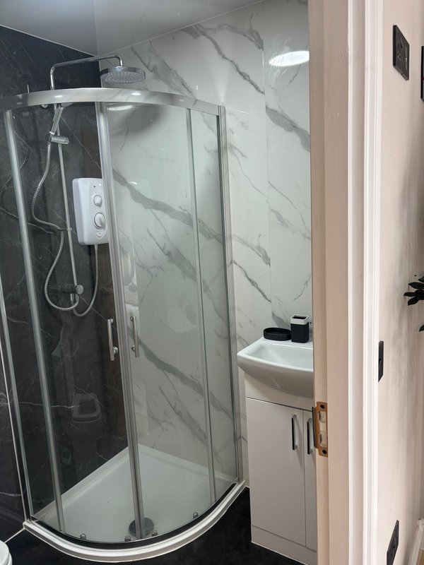 Modern bathroom with curved glass shower enclosure, marble-effect tiling, and white vanity unit