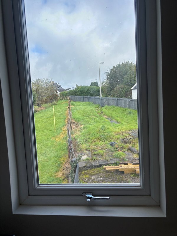 Garden view through window showing green lawn, fencing, and trees beyond