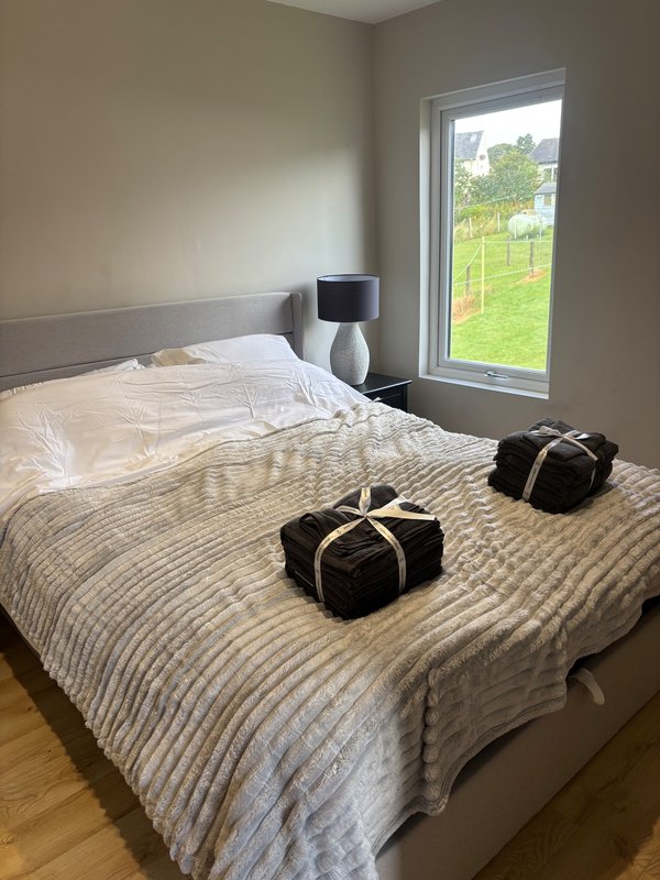 Modern bedroom with double bed, striped bedding, gray headboard, bedside lamp and garden view