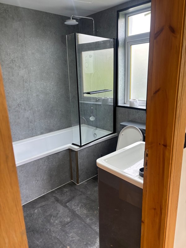 Modern bathroom with walk-in shower, white bathtub, grey tile walls and window