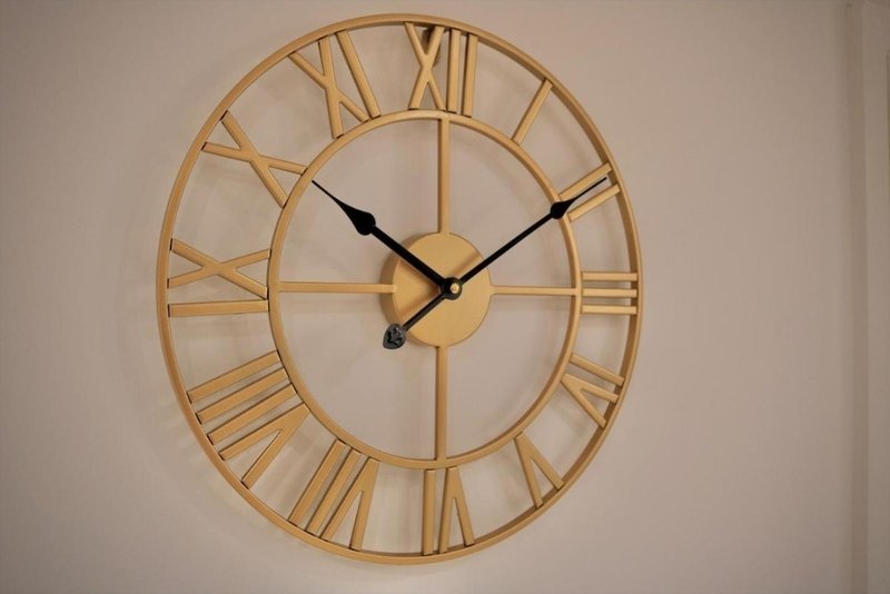 Large golden wall clock with Roman numerals and black hands on white wall