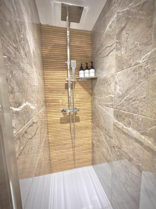 Modern shower enclosure with marble-effect tiles, wooden slat accent wall, rainfall showerhead and shelf with toiletries