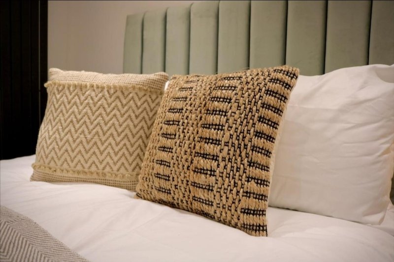 Bed with decorative cushions and cream bedding against upholstered headboard