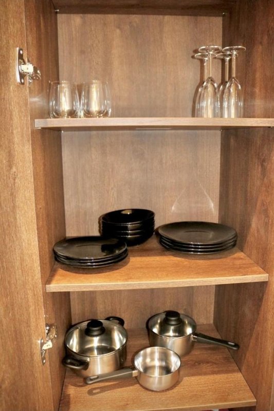 Kitchen cabinet interior with shelves displaying glasses, plates, and stainless steel cookware