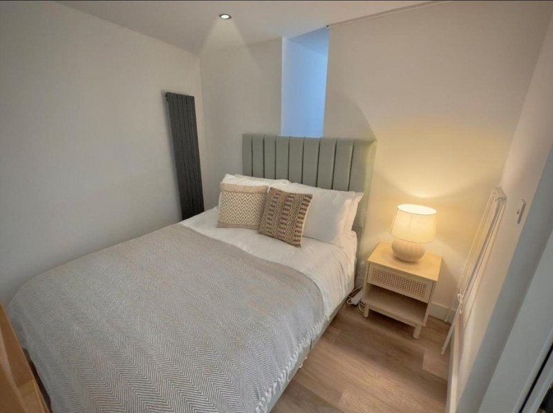 Bedroom with double bed, green headboard, bedside lamp and wooden flooring