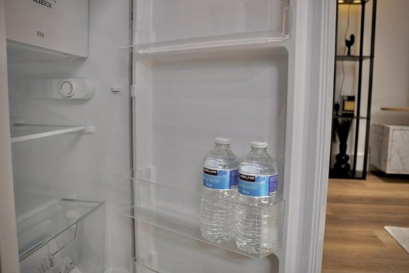 Open refrigerator with bottled water inside, kitchen visible in background