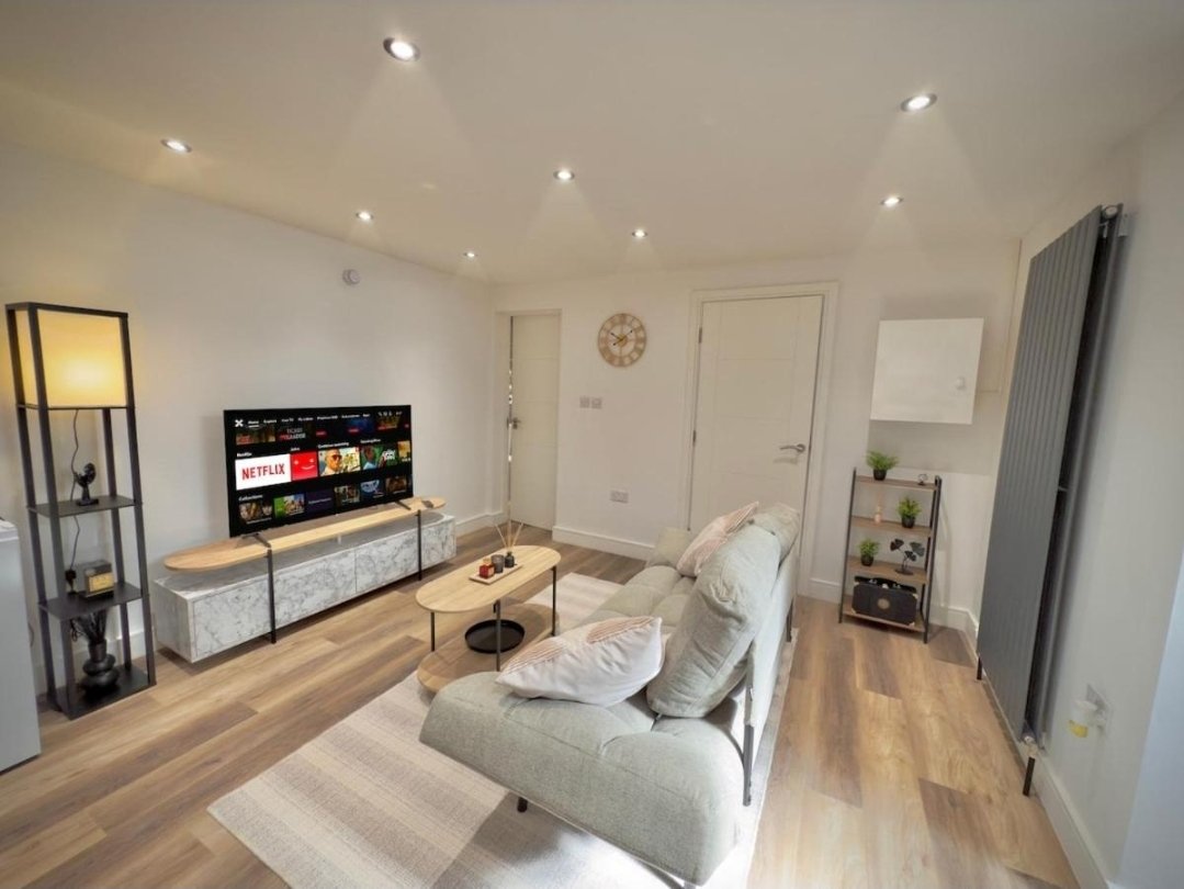 Modern living room with grey sofa, TV unit, wooden flooring, and recessed ceiling lights