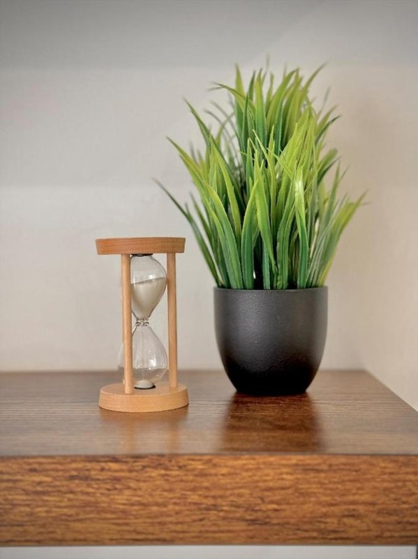 Wooden table with hourglass and potted green plant against white wall