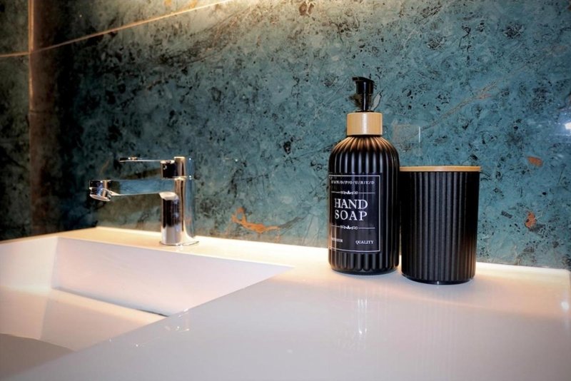 Modern bathroom sink with hand soap dispenser and accessories against textured blue-green wall