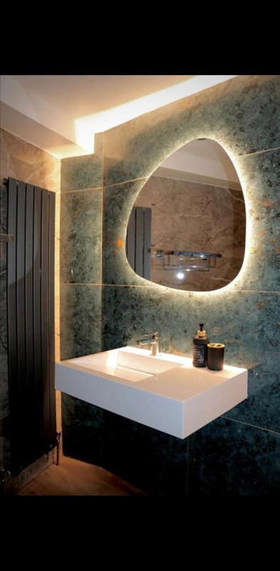 Modern bathroom with illuminated round mirror, white sink, and textured green tile walls