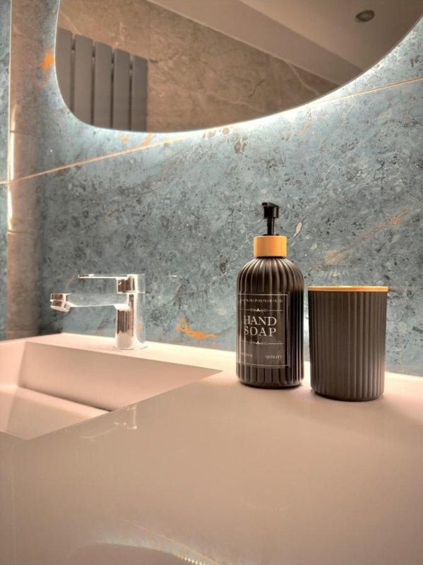 Modern bathroom with curved mirror, marble wall, white sink and hand soap dispenser
