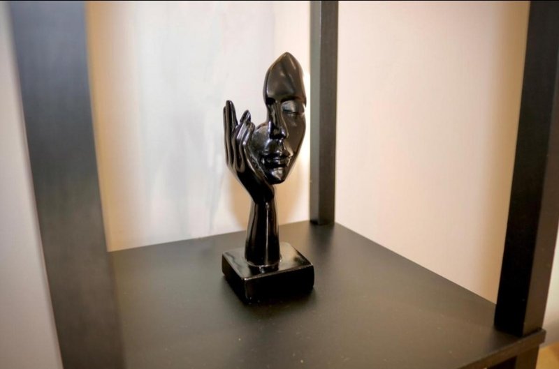 Black sculptural ornament displayed on dark shelf against white wall